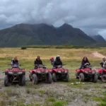 A group of tourists on ATVs ready for an adventure near Maras and Moray, in Cusco, Peru. People wearing helmets pose in an Andean countryside under a cloudy sky, with green mountains in the background. An exciting experience that combines nature, Inca history, and fun in the Sacred Valley.