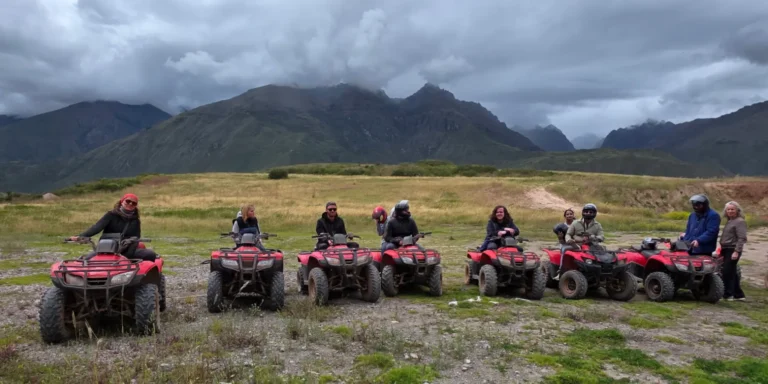 A group of tourists on ATVs ready for an adventure near Maras and Moray, in Cusco, Peru. People wearing helmets pose in an Andean countryside under a cloudy sky, with green mountains in the background. An exciting experience that combines nature, Inca history, and fun in the Sacred Valley.
