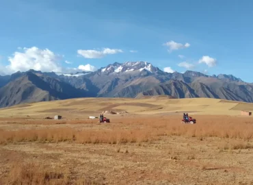 Tourists on ATVs tour a vast Andean countryside near Maras and Moray, in Cusco, Peru. Two vehicles travel across a vast, dry plain under a blue, cloudy sky, with snow-capped mountains in the background. A thrilling adventure experience amidst the stunning landscapes of the Sacred Valley.