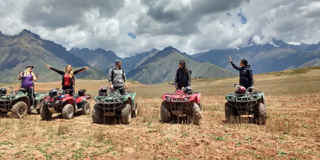 A group of tourists on ATVs posing in an Andean countryside near Maras and Moray, in Cusco, Peru. People wearing helmets celebrate the adventure in front of green mountains and a cloudy sky. An exciting experience that combines nature, history, and fun in the Sacred Valley.
