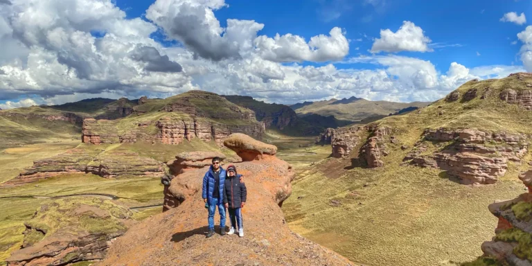 Formação rochosa no Cânion Tinajani, Peru. Casal posando em uma rocha em forma de cogumelo em meio a uma paisagem andina espetacular. Vista panorâmica do cânion com montanhas erodidas, vales verdes e céu azul. Um destino natural em Puno, ideal para caminhadas e exploração das maravilhas geológicas do Altiplano.