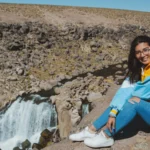 Viajante posando em frente às Cataratas de Pillones, Peru – uma cachoeira natural no planalto andino com paisagens rochosas e um rio entre montanhas no sul do país.