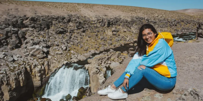 Viajante posando em frente às Cataratas de Pillones, Peru – uma cachoeira natural no planalto andino com paisagens rochosas e um rio entre montanhas no sul do país.