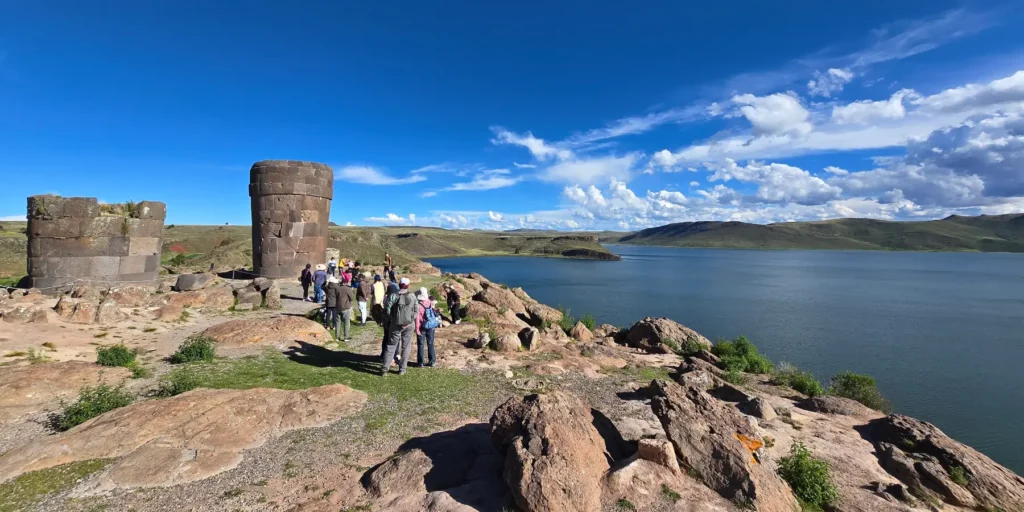 Vista panorámica de Sillustani, Perú. Chullpas preincaicas de piedra junto al Lago Umayo, con turistas explorando el sitio arqueológico. Sitio cultural de la cultura Colla, ubicado en Puno, ideal para disfrutar de la historia andina y la naturaleza del altiplano.