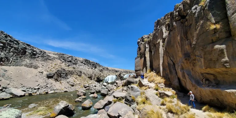 Cachoeira Pillones no sul do Peru – viajantes caminham por um cânion com cachoeiras naturais, rochas e um rio entre as montanhas do planalto andino.