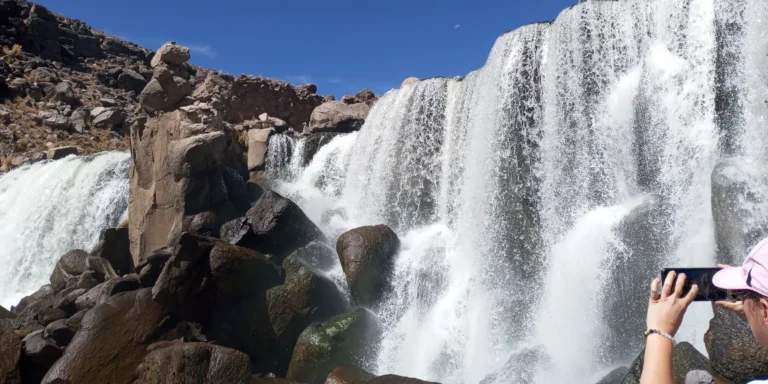 Cachoeiras de Pillones, no planalto andino do Peru – uma viajante tirando fotos com seu celular das cachoeiras naturais entre as rochas e montanhas no sul do país.