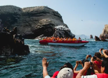Tourists in red boats enjoying a tour of the Ballestas Islands, Peru. People wearing life jackets observe and take photos as they sail among rocky cliffs and seabirds. An exciting trip to see wildlife in the Peruvian Pacific.