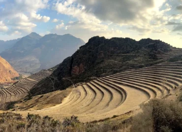 Inca agricultural terraces in Pisac, Cusco, Peru. Large circular terraces carved into the mountainsides, built by the Incas to grow food. In the background, mountains and valleys under a cloudy sky, showcasing the engineering and agricultural wisdom of the Inca civilization.