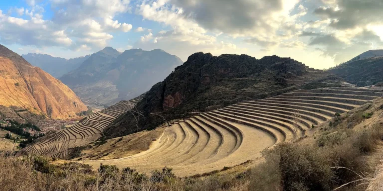 Inca agricultural terraces in Pisac, Cusco, Peru. Large circular terraces carved into the mountainsides, built by the Incas to grow food. In the background, mountains and valleys under a cloudy sky, showcasing the engineering and agricultural wisdom of the Inca civilization.