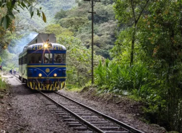 Trens da Peru Rail serpenteiam pelas montanhas em direção a Machu Picchu, Peru. Vagões coloridos com grandes janelas percorrem um vale cercado por vegetação exuberante e rios, oferecendo aos passageiros vistas espetaculares da paisagem andina. Uma maneira confortável e segura de viajar entre Cusco e a cidadela inca.
